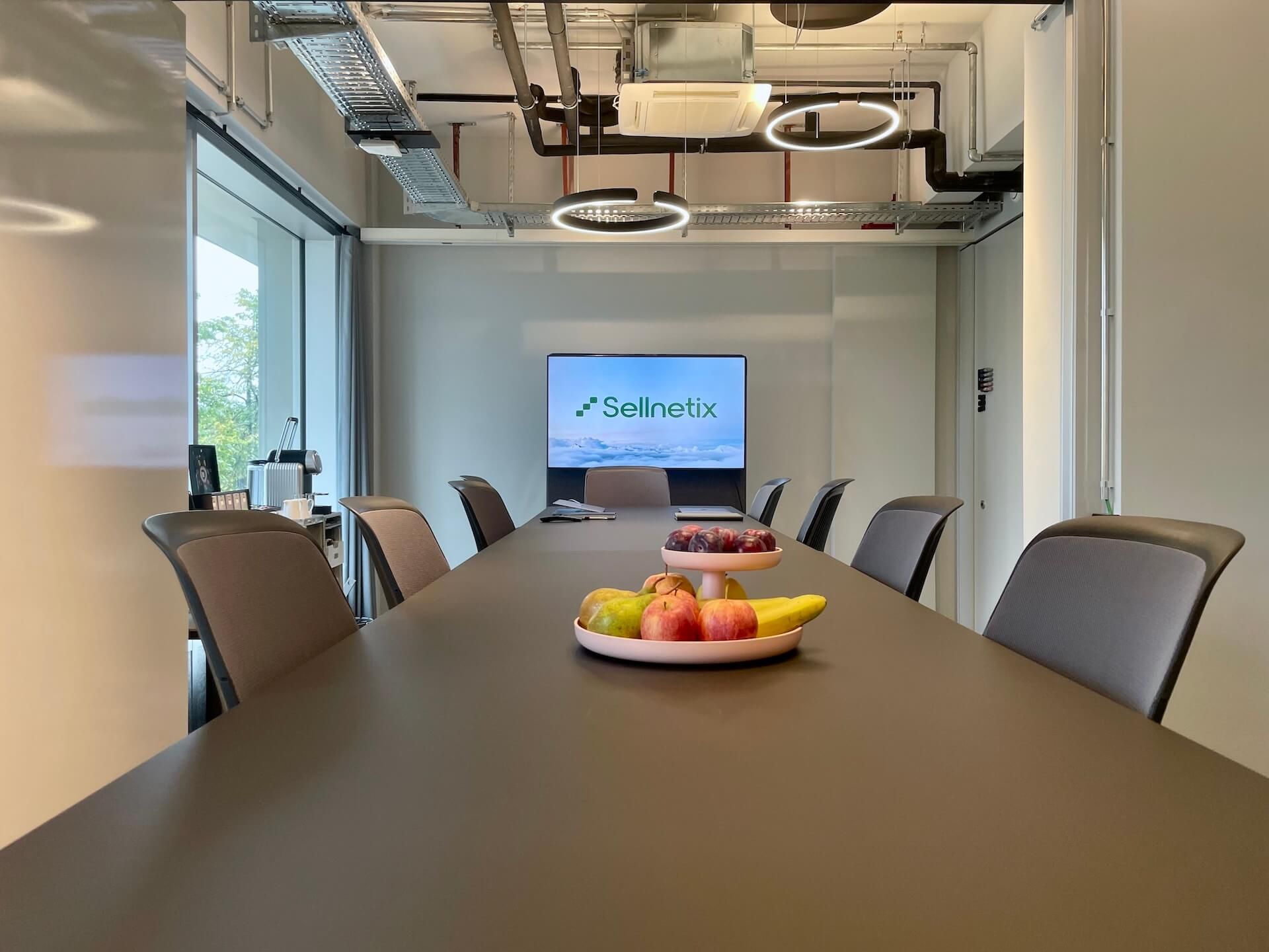 Besprechungsraum von Sellnetix: langer Tisch, Obstschale und ein Bildschirm mit dem Sellnetix-Logo